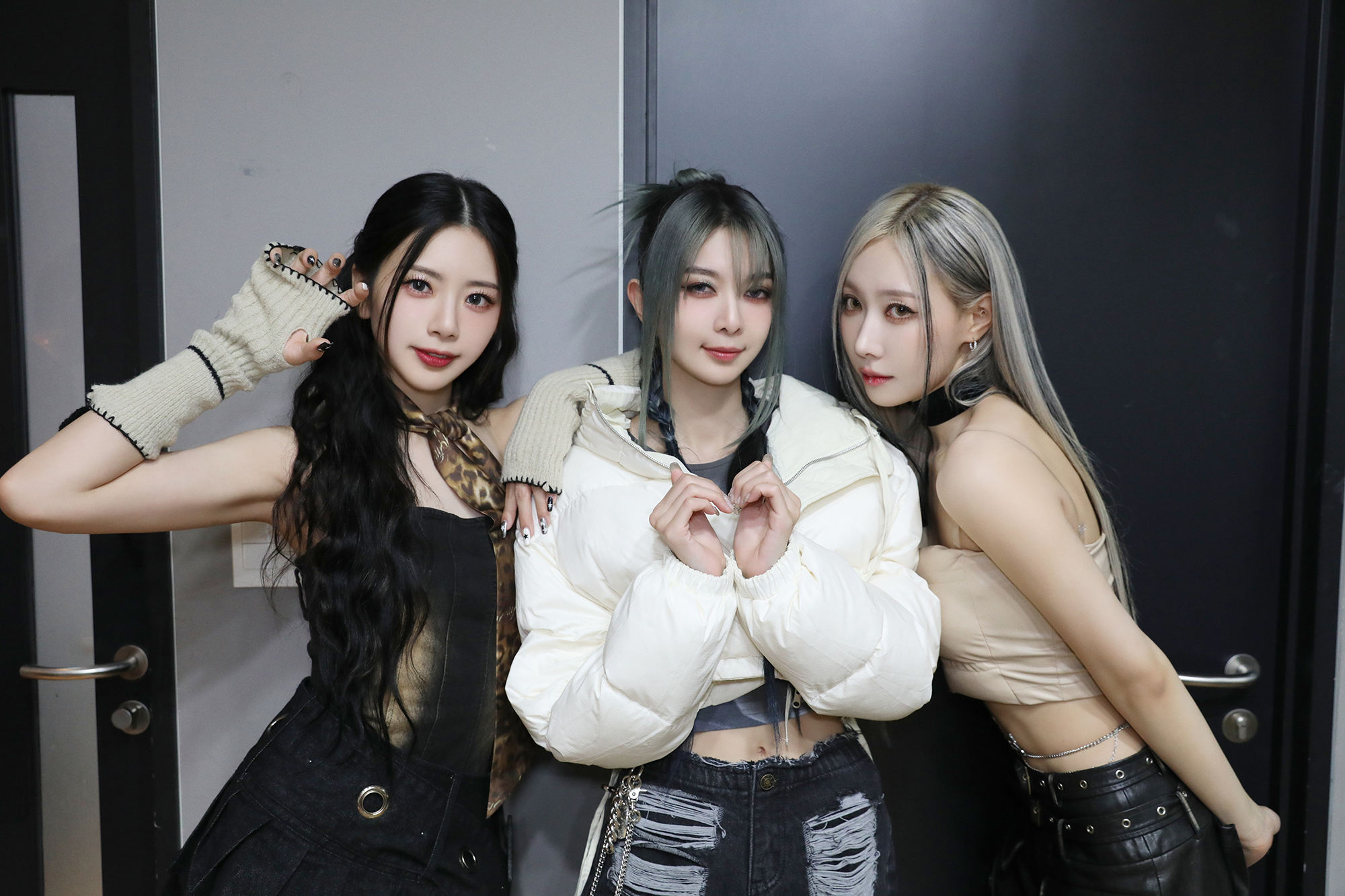 JiU, Dami, and Handong look into the camera with a heart pose for a music show.