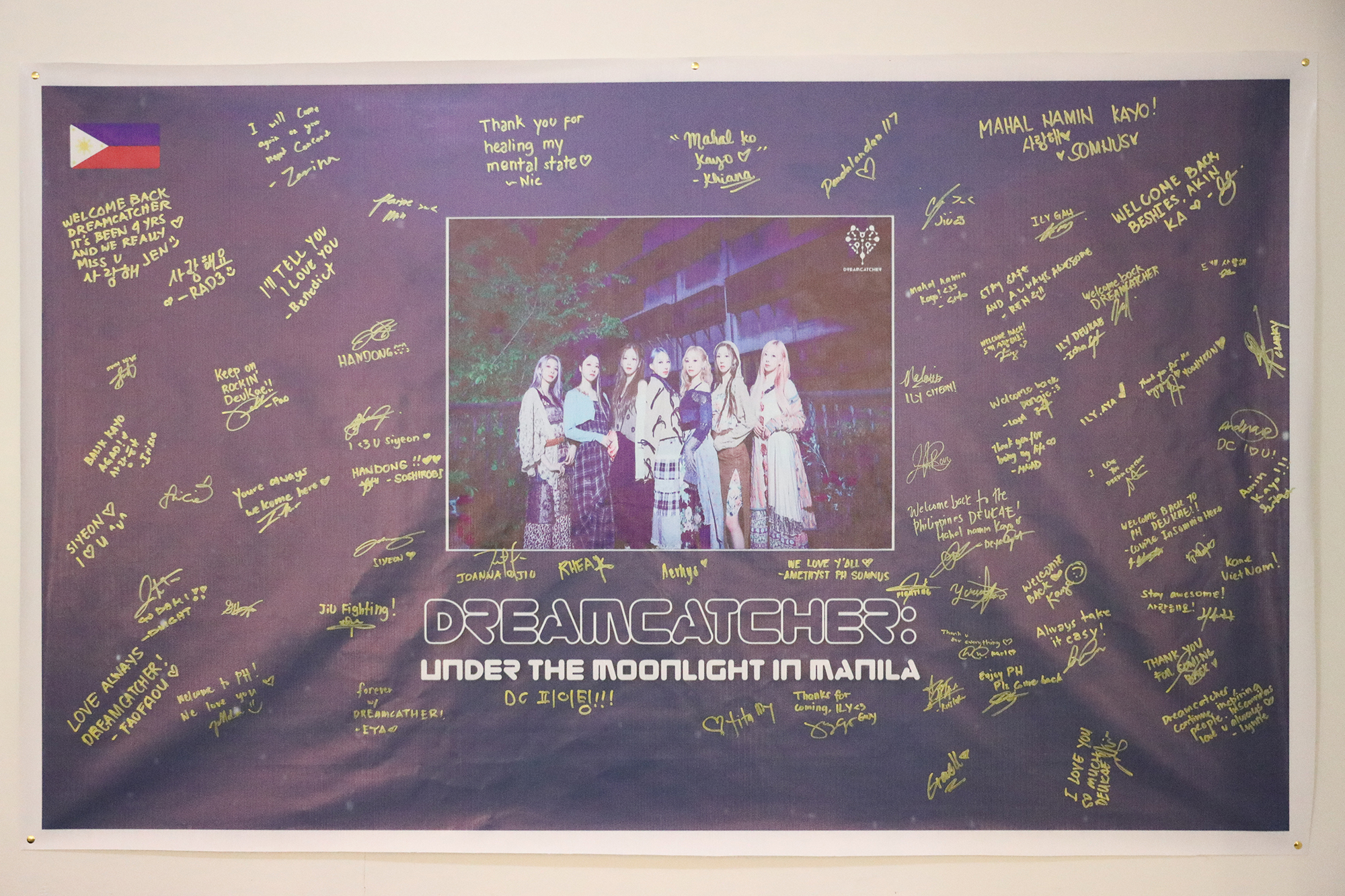 Black banner with Dreamcatcher under the moonlight picture on it signed by fans.